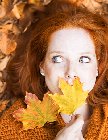 Frau mit roten Haaren liegt auf vielen bunten Blättern im Herbst